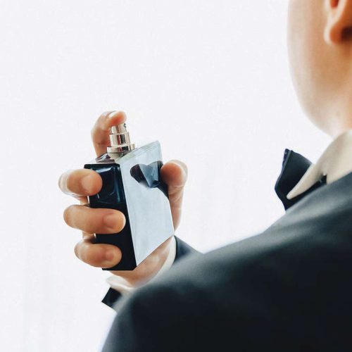 مدل مرد با لباس مشکی در حال نگهداری شیشه عطر ادوپرفیوم مردانه آرمانی با پسزمینه خاکستری روشن
