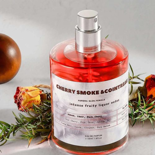 بطری عطر Cherry Smoke Cointreau با مایع قرمز رنگ و برچسب مشخصات نتهای بویایی آلبالو، دود، بادام و وانیل در کنار رز خشکشده